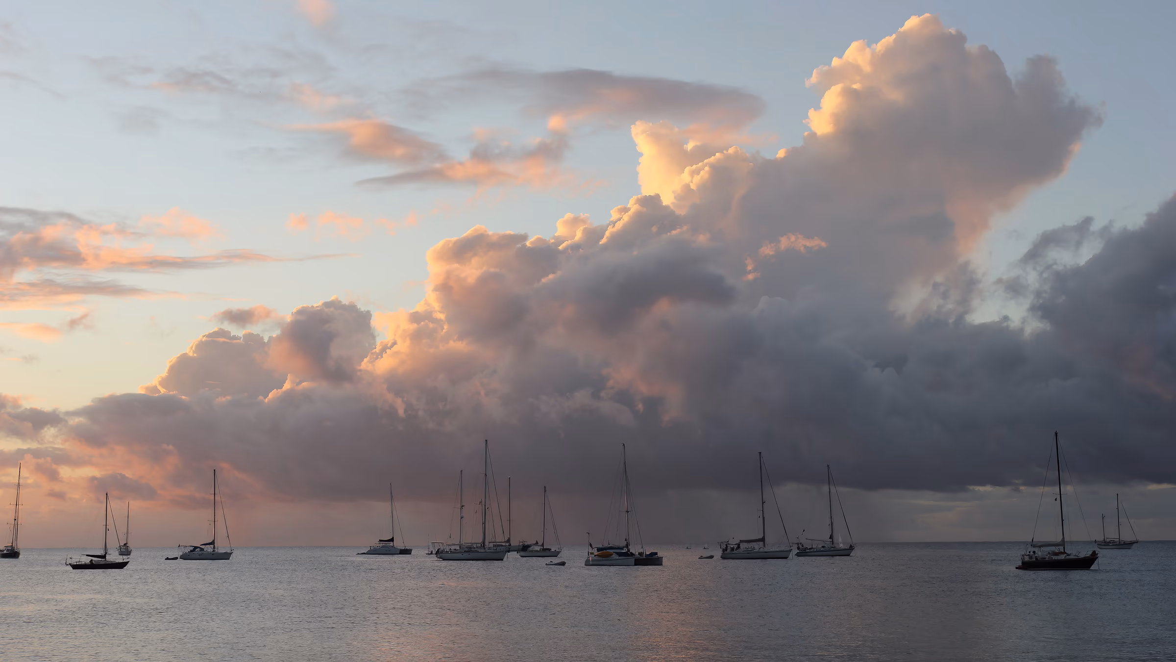 Sailboat masts silhouetted in a quiet anchorage under gold-lit evening clouds.